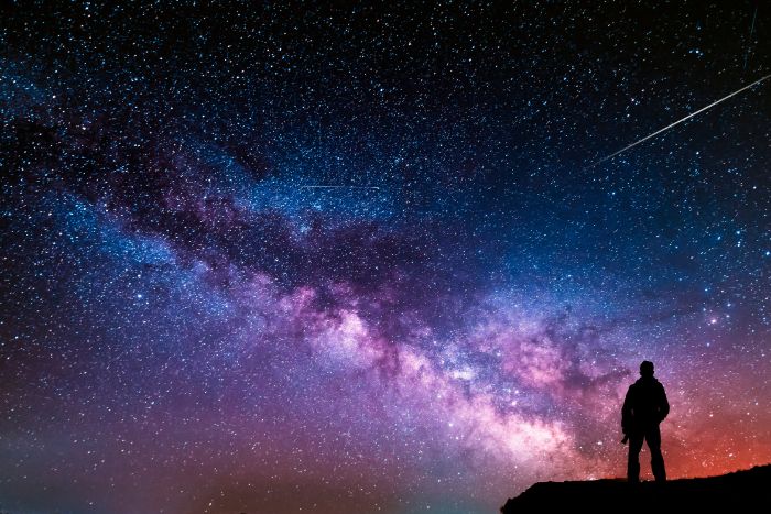 Small silhouette of a person standing against the night sky as if to represent the enormity of the universe